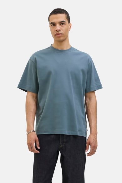 T-shirt bleu à manches courtes de CORE BY JACK & JONES, porté avec un bracelet en argent et des jeans foncés.