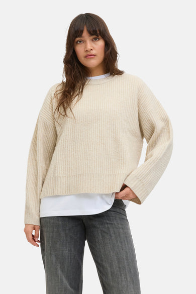 Pull beige à col rond de JJXX porté sur un t-shirt blanc et des jeans gris.