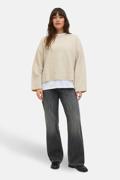 Gilet rond beige de JJXX porté sur un shirt blanc, avec des jeans noirs et des chaussures noires.