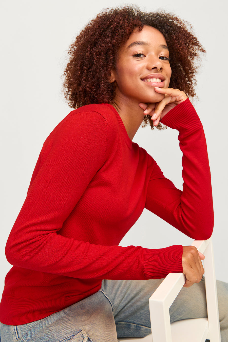 T-shirt rouge avec col rond de JJXX, modèle assis avec cheveux bouclés bruns et jeans bleus.