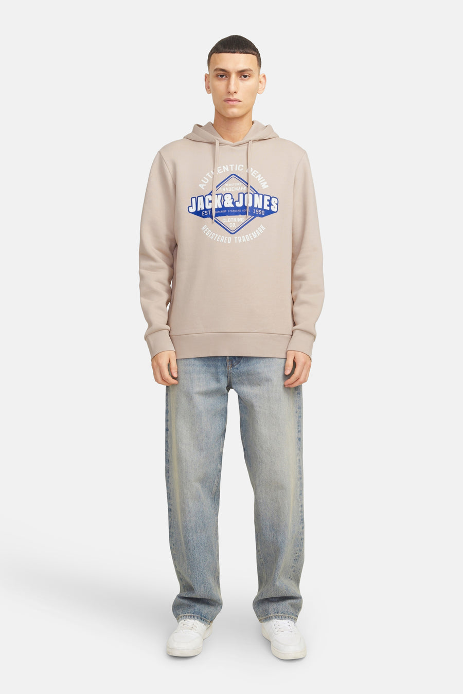 Pull beige à capuche de ORIGINALS BY JACK & JONES, avec imprimé logo bleu sur le devant, combiné avec un jean décontracté et des baskets blanches.