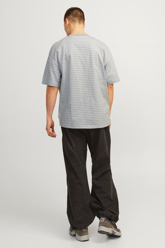 Een man van achteren, draagt een gestreept grijs shirt, zwarte broek en sportschoenen.