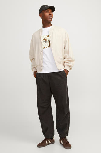 T-shirt blanc à manches courtes d'ORIGINALS BY JACK & JONES, avec une impression sur la partie avant, associé à un bomberjack beige et un pantalon noir.