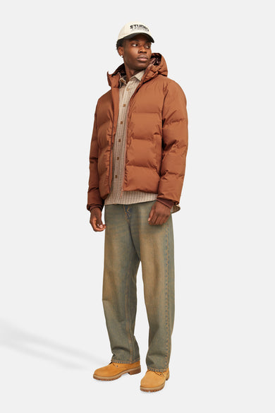 Veste de pluie marron de CORE BY JACK & JONES, portée avec un chemisier à carreaux, des jeans décontractés et des chaussures en cuir.
