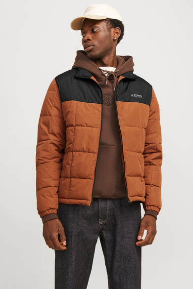 Bruine korte jas van CORE by JACK & JONES, met zwarte schouderpas, gedragen over een bruine hoodie en donkere jeans.