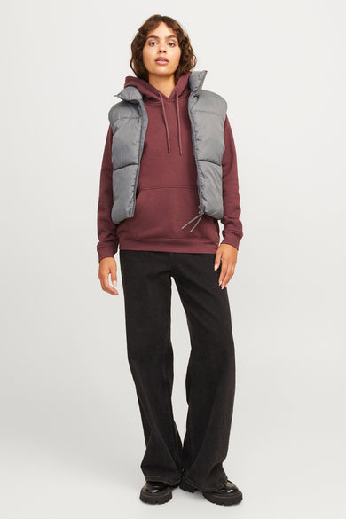 Grijze bodywarmer van JJXX, gestyled met een bordeauxrode hoodie en zwarte jeans.
