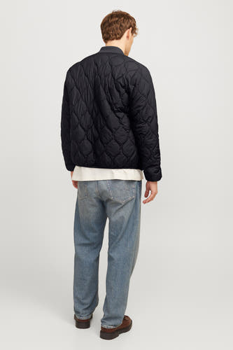 Manteau court noir de PREMIUM BLUE par JACK & JONES, avec un motif de carreaux intégré et porté avec un chemisier blanc et des jeans bleus.