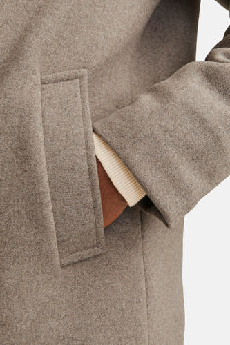 Manteau long beige de PREMIUM par JACK & JONES, avec une main dans la poche et un pull crème en dessous.