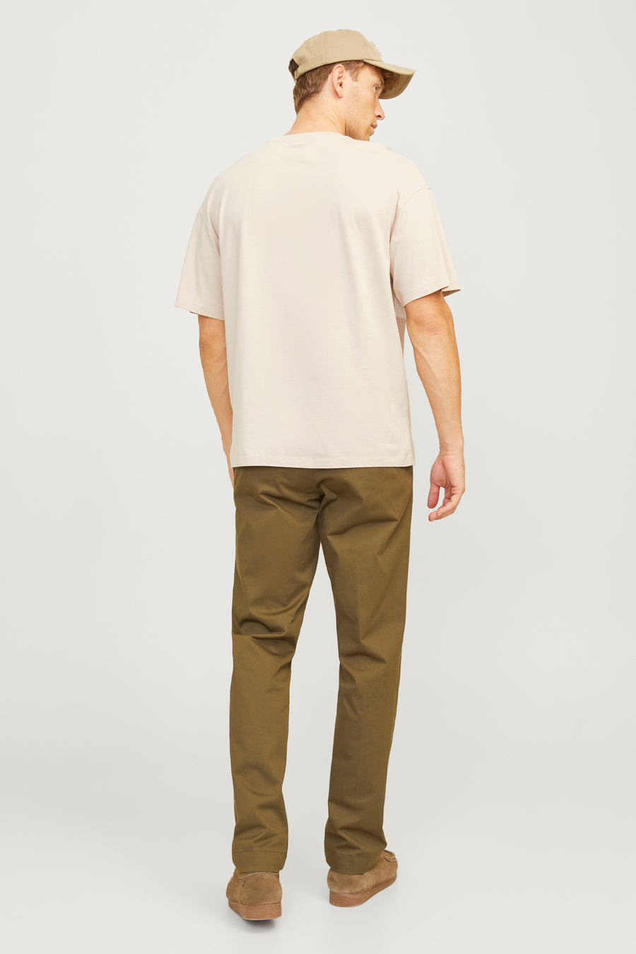 Man van achteren, beige shirt, olijfgroene broek, suède schoenen.