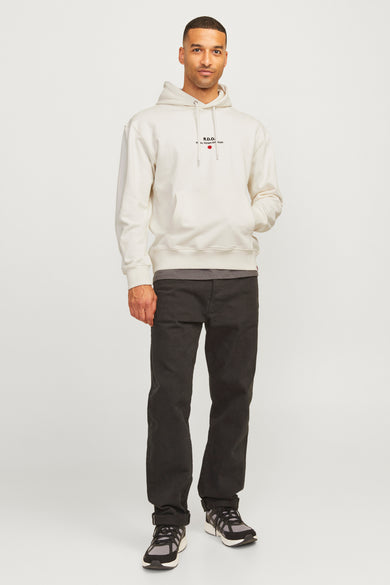 Ecru sweater met cap van Royal Denim Division, met een logo op de borst, gecombineerd met zwarte jeans en sneakers.
