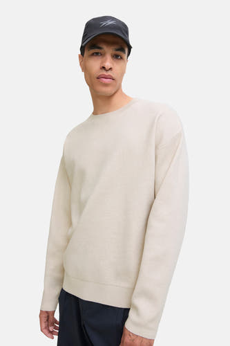 Pull beige à col rond de PREMIUM by JACK & JONES, porté avec un chapeau noir et des pantalons foncés.