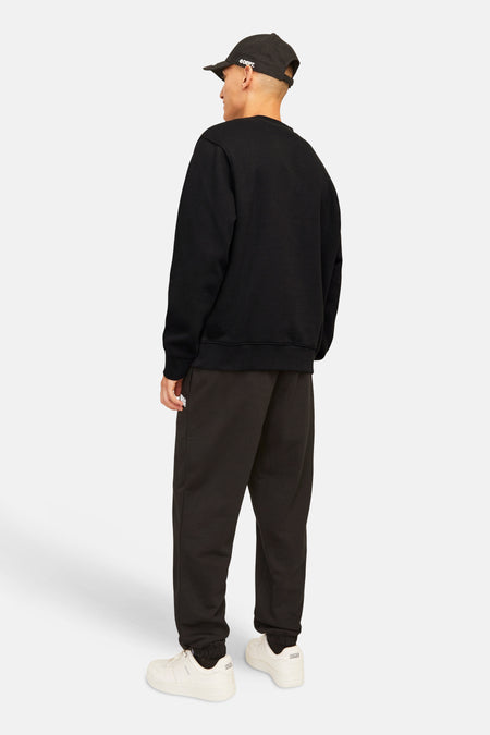 Pull noir à col rond de ORIGINALS BY JACK & JONES, vu de dos, combiné avec une casquette noire et un jogging marron.
