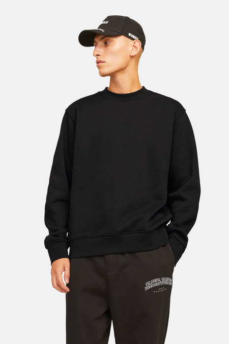 Sweat-shirt noir de ORIGINALS BY JACK & JONES, à manches longues et col rond, porté avec un jogging et une casquette.