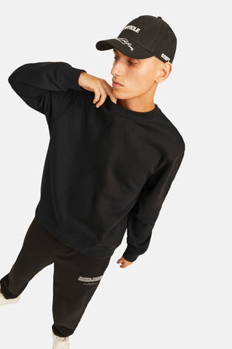 Pull noir à col rond de ORIGINALS BY JACK & JONES, porté avec une casquette noire et un jogging noir.