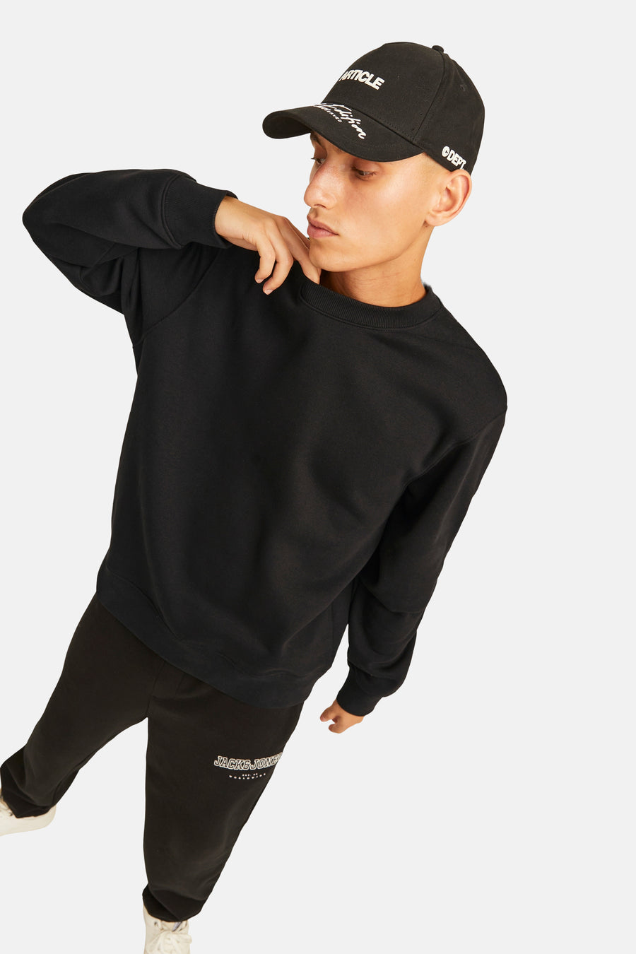 Pull noir à col rond de ORIGINALS BY JACK & JONES, porté avec une casquette noire et un jogging noir.