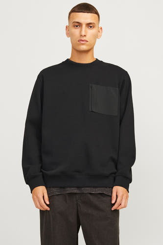 Pull-over noir de CORE BY JACK & JONES, avec poche poitrine et porté avec un pantalon sombre et des baskets.