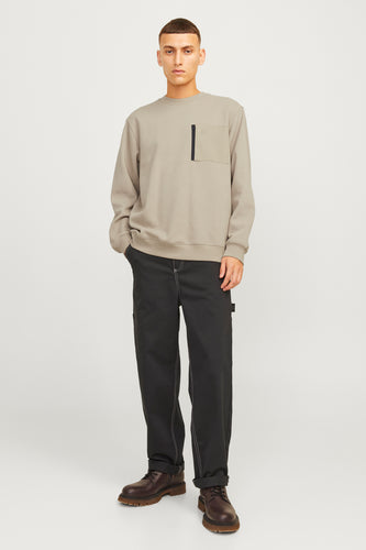 Man in beige sweater, zwarte broek en bruine schoenen.