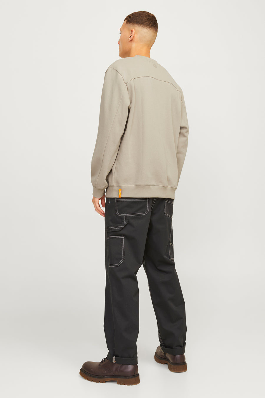 Man achterkant, grijze trui, zwarte broek, bruine schoenen.