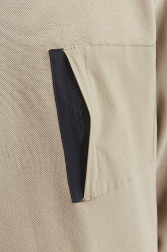 Beige trui met zak en zwarte ritssluiting.
