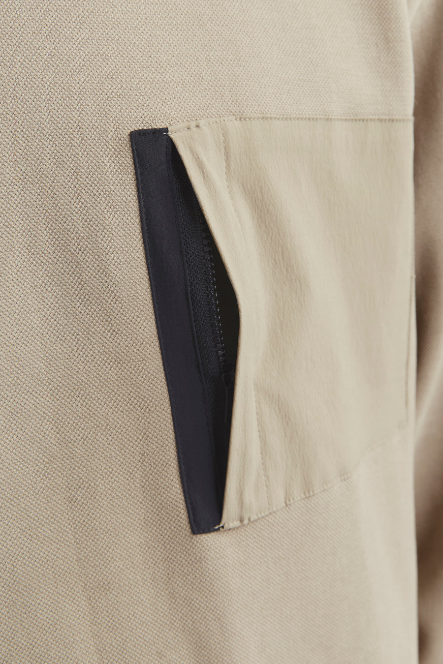 Beige trui met zak en zwarte ritssluiting.
