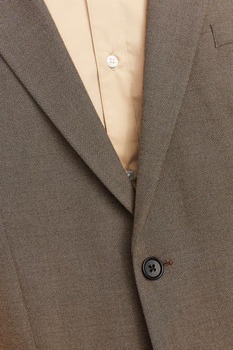 Blazer gris de PREMIUM par JACK & JONES, avec un motif subtil et une seule boutonnière, porté sur une chemise claire.