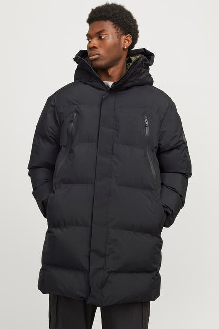 Manteau long noir de CORE BY JACK & JONES avec poches à fermeture éclair et capuche, porté avec un pantalon.