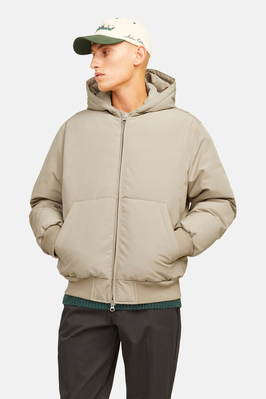 Veste courte beige de CORE BY JACK & JONES avec motif à carreaux subtil, capuche, fermeture éclair, poignets côtelés et poches latérales, portée par un mannequin avec une casquette.