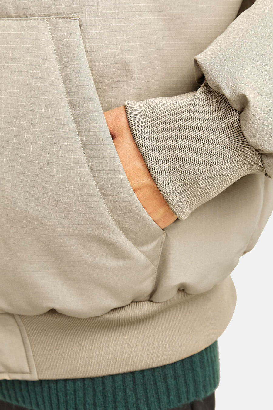 Manteau court beige de CORE BY JACK & JONES avec texture ripstop, poignets côtelés et poche pour les mains, porté sur un pull vert.