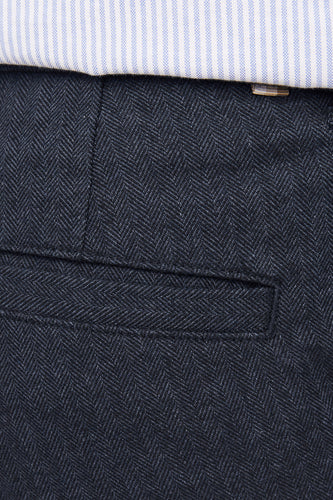 Blauw geruit overhemd boven donkerblauwe visgraat broek met zak.
