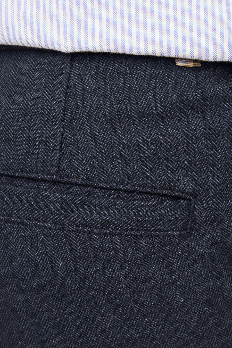 Blauw geruit overhemd boven donkerblauwe visgraat broek met zak.
