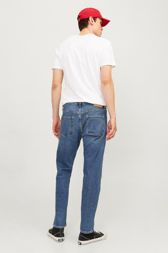 Jean tapered bleu de JACK & JONES JEANS INTELLIGENCE, avec des poches arrière, porté avec un T-shirt blanc et des baskets noires.
