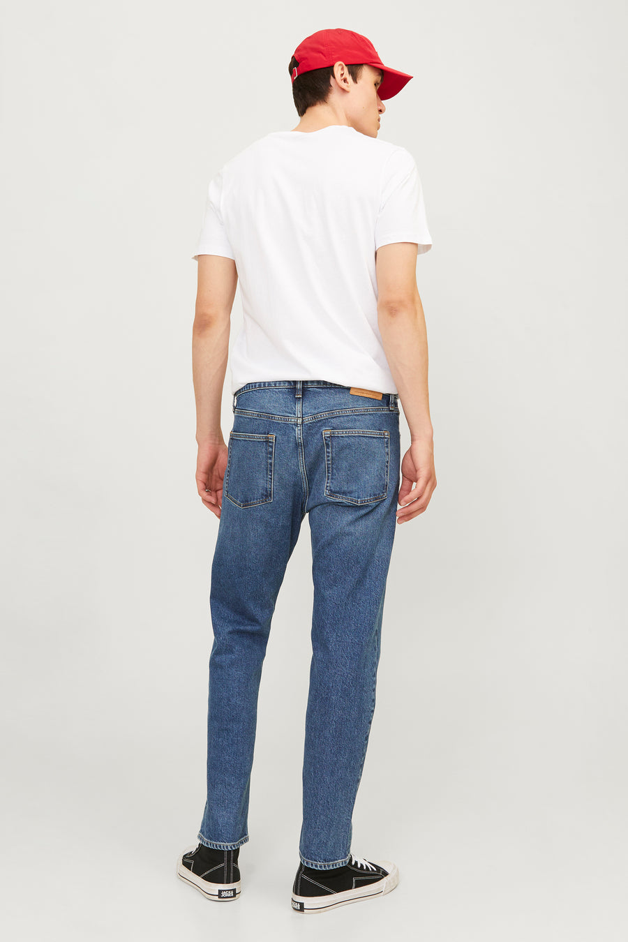 Achteraanstaande man in witte T-shirt, blauwe jeans, rode pet en zwarte sneakers.