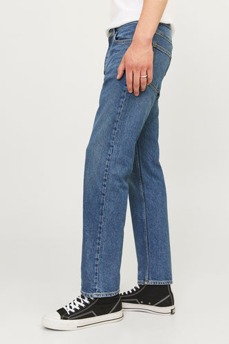 Staande man in blauwe jeans en zwarte sneakers.