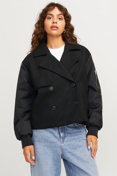 Manteau court noir de JJXX, porté avec un chemisier blanc et des jeans bleus larges.
