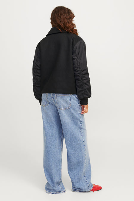Manteau court noir de JJXX, avec des manches longues et porté avec des jeans larges et des chaussures rouges.