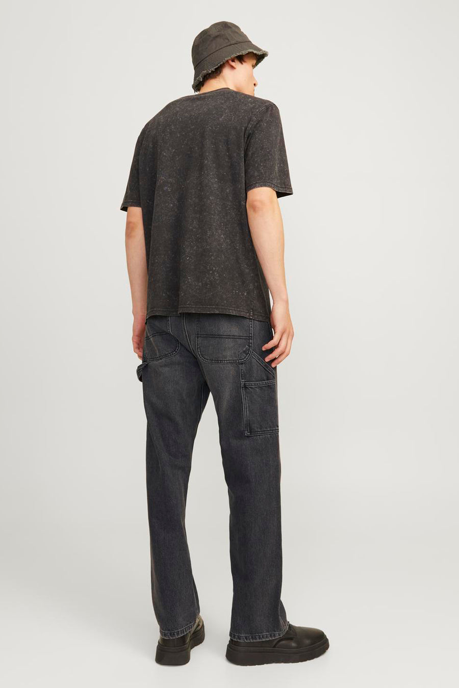 Jean délavé noir de JACK & JONES JEANS INTELLIGENCE, avec des poches à outils, associé à un T-shirt noir et un chapeau bucket.