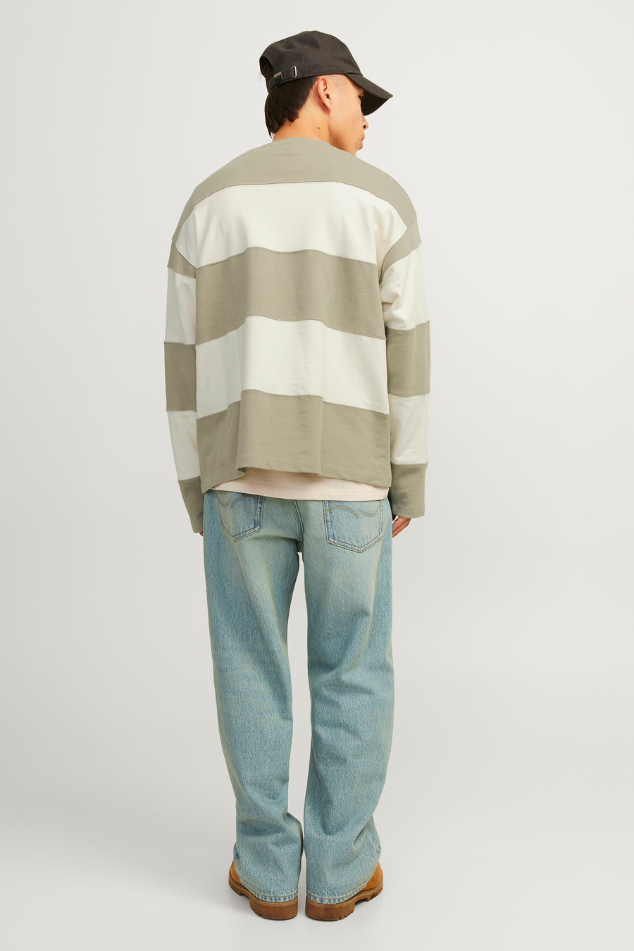 Man van achteren, gestreept shirt, blauwe jeans, bruine schoenen, grijze pet.
