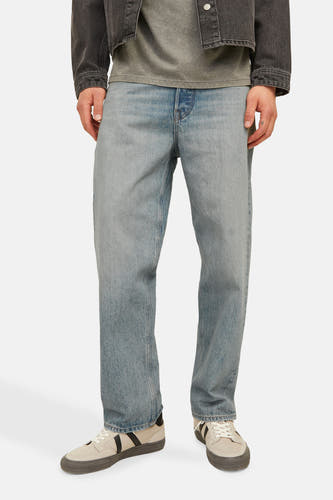 Jean décontracté de denim bleu clair de JACK & JONES JEANS INTELLIGENCE, avec une coupe décontractée et porté avec des baskets et un manteau foncé.