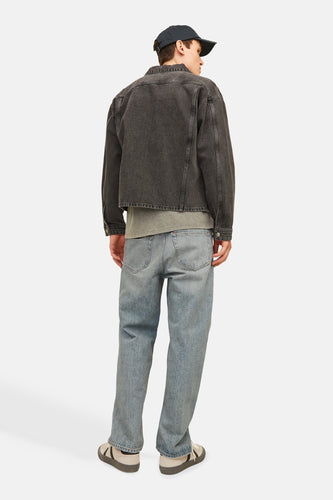 Man van achteren met zwarte denimjas, blauwe jeans en sneakers tegen witte achtergrond.