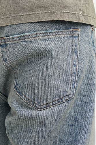 Close-up van een denim broek met achterzak, lichtblauw, met een grijze top.