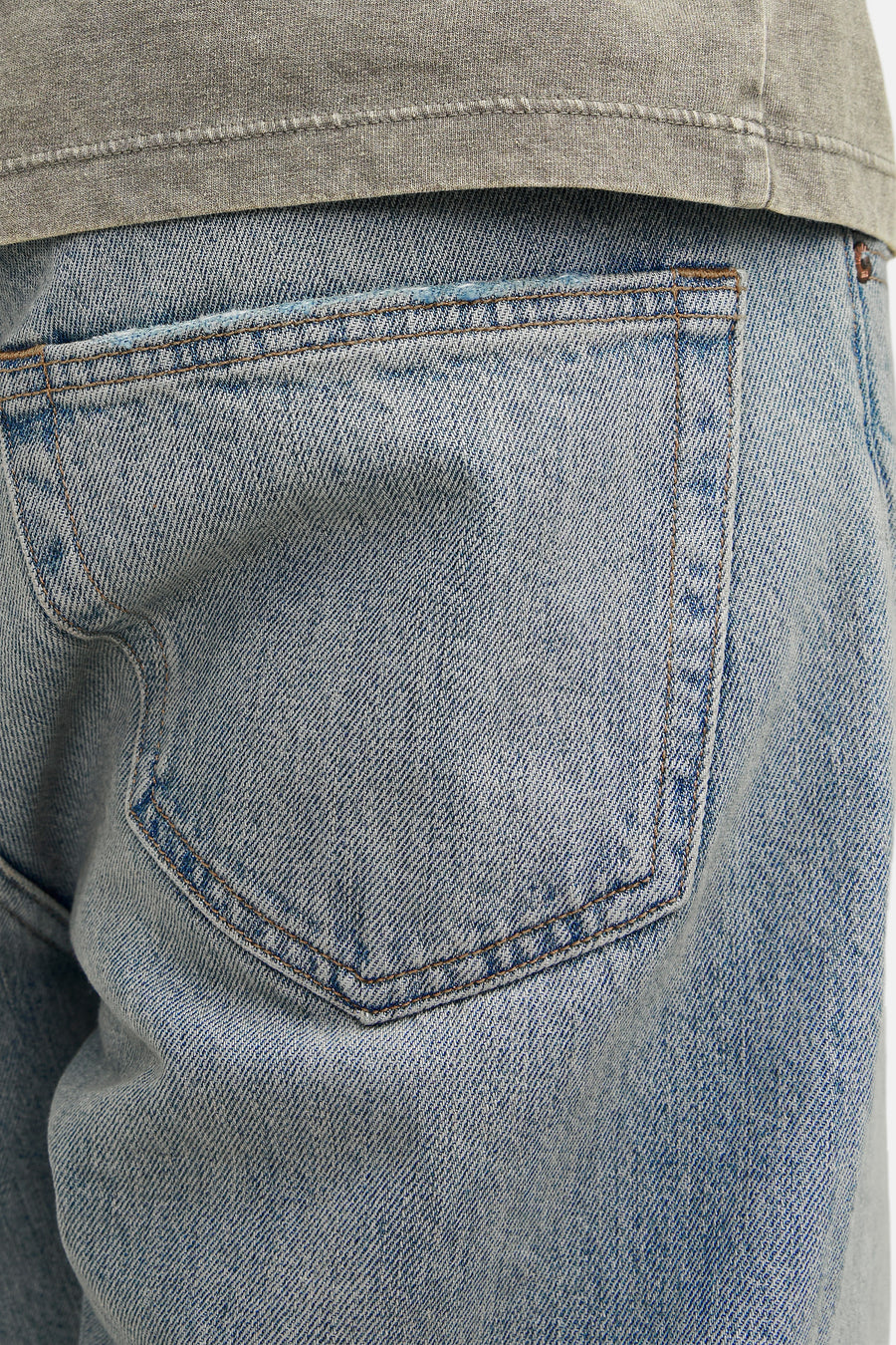 Close-up van een denim broek met achterzak, lichtblauw, met een grijze top.