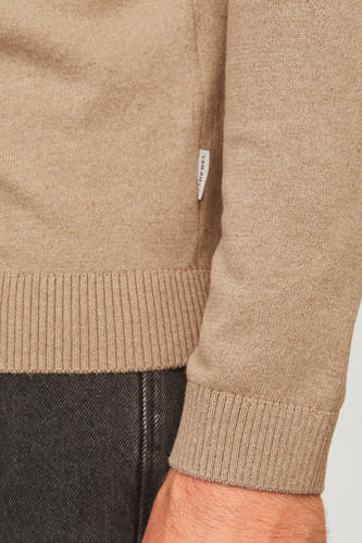 Pull beige à col rond de JJREBEL, avec des manches longues et des bordures côtelées, partiellement visible avec des jeans foncés.