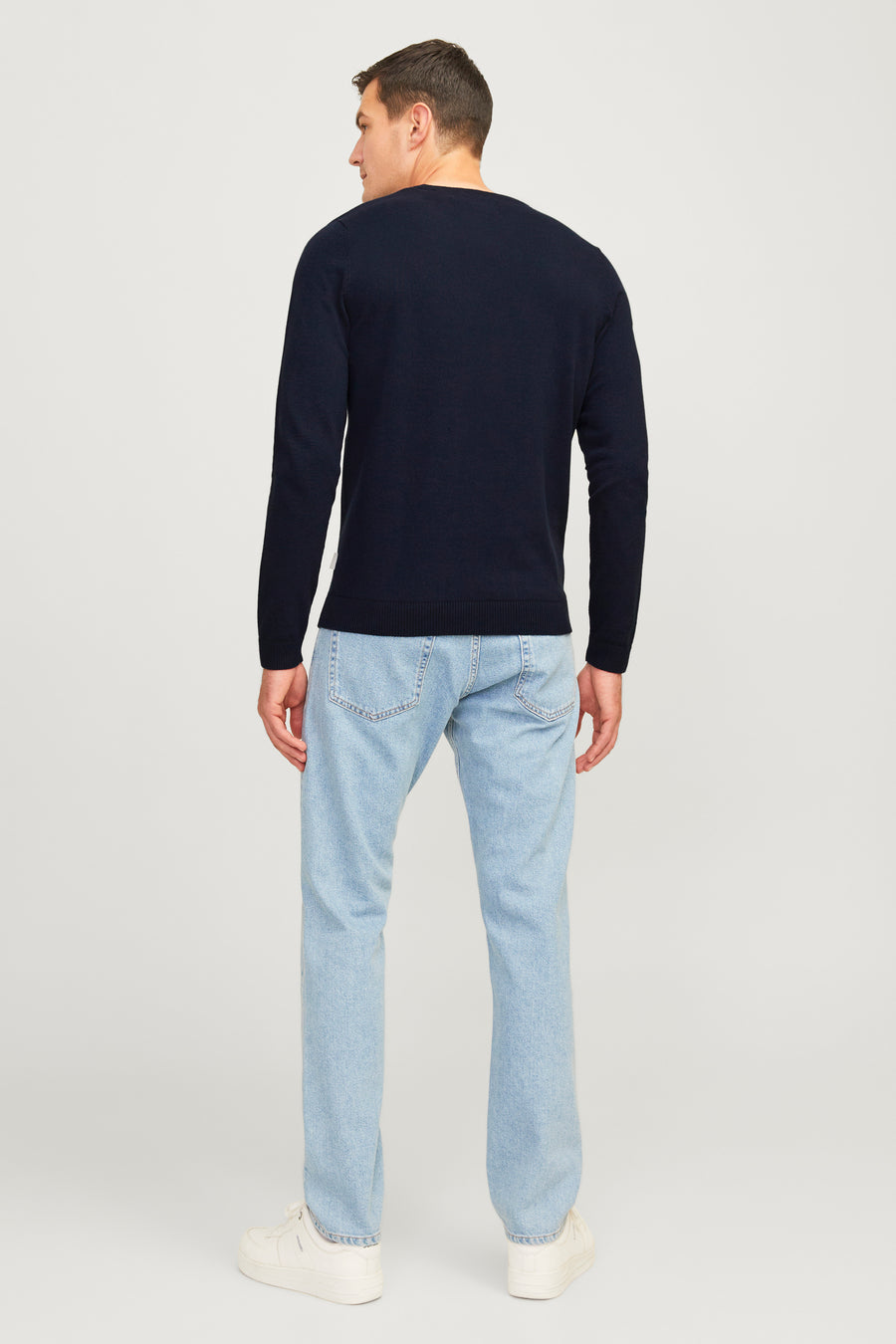 Blauwe trui met ronde hals van JJREBEL, op de rug gezien, gecombineerd met lichtblauwe jeans en witte sneakers.