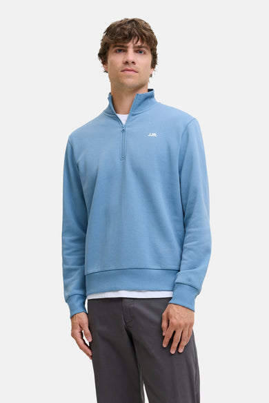 Pullau bleu JJREBEL, avec une courte fermeture éclair et porté sur un T-shirt blanc avec un pantalon gris.