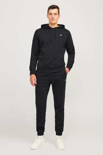 Jean jogging noir de JJREBEL, associé à une hoodie noire, des chaussettes blanches et des baskets crème.