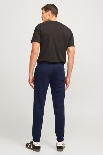 Blauwe joggingbroek van JJREBEL, gezien van achteren, gecombineerd met een zwart T-shirt en bruin-witte sportschoenen.
