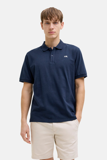 Polo bleue de JJREBEL, à manches courtes et portée avec un short beige et des sandales marron.
