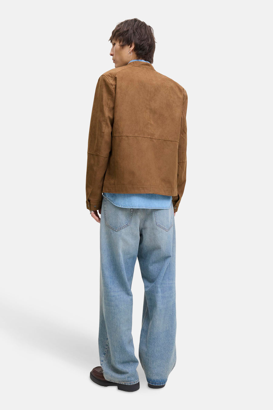 Achterkant van een man in bruine jas, lichtblauw overhemd en wijde jeans.