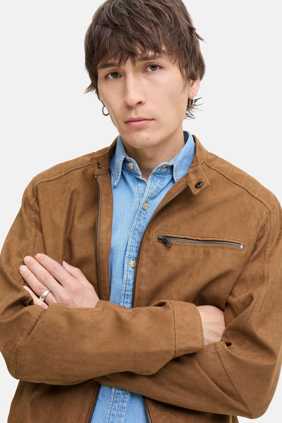 Man met gekruiste armen, bruine jas en blauw overhemd.
