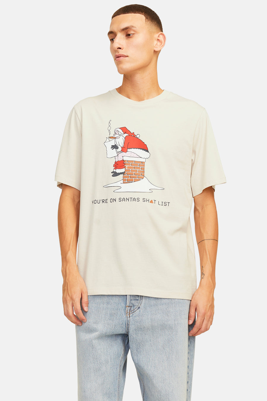 Man in beige T-shirt met Santa print, blauwe jeans.